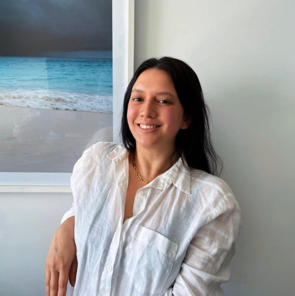 Mel Sanchez sonriendo junto a una obra con paisaje de playa